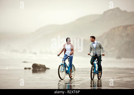Felice coppia giovane la bicicletta lungo una spiaggia con la bassa marea. Foto Stock