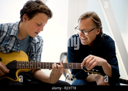 Metà uomo adulto insegnando un ragazzo adolescente dove mettere le dita sulla tastiera durante una lezione di chitarra. Foto Stock