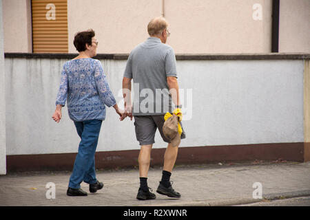 Il tedesco antico popolo amante camminando mano nella mano camminando sul marciapiede accanto alla strada andare alla stazione dei bus a Sandhausen villaggio sul 25 agosto 2017 in Heidelberg, Foto Stock