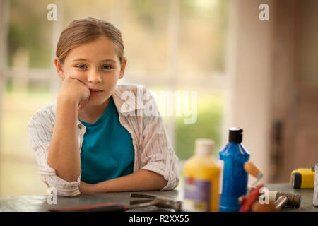 Ritratto di una ragazza contemplativa appoggiato su un banco di lavoro pieno di strumenti artigianali all'interno di un garage. Foto Stock