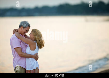 Coppia matura sorridente e abbracciando sulla spiaggia al tramonto. Foto Stock
