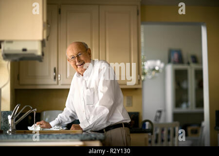 Sorridente uomo anziano pulisce fino in cucina dopo pranzo. Foto Stock