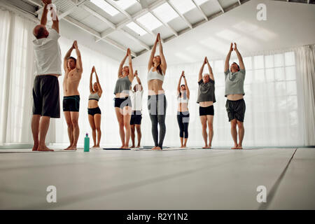 La gente lo stiro con le braccia sollevate durante una lezione di yoga. Foto Stock