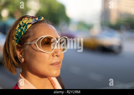 Ritratto di fiduciosa matura donna Taiwanese di etnia cinese guardando in lontananza la sera sun contro la grande città sullo sfondo del traffico Foto Stock