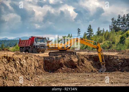 Escavatore giallo e il carrello vuoto il lavoro presso il sito in costruzione Foto Stock