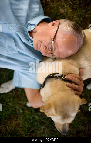 Senior uomo disteso sul prato con il suo cane. Foto Stock