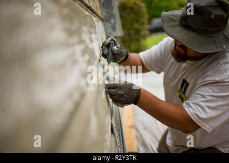 Lavoratore di raschiatura off di vernice di una vecchia casa a spiovente. Foto Stock