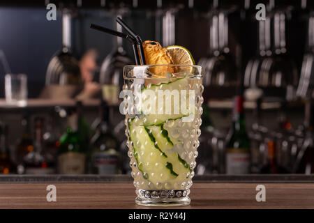 Bicchiere di gin tonic cocktail decorata con il cetriolo a bat sfondo del contatore. cocktail sorge sulla barra Foto Stock