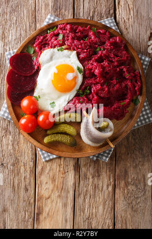 La cucina tedesca Labskaus è una purea di patate, corned beef e barbabietola con uovo fritto, cetrioli sottaceto e rollmop close-up su una piastra. Verticale in alto v Foto Stock