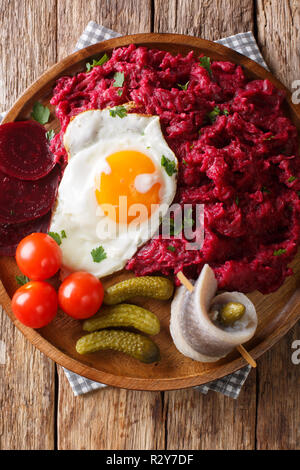 Labskaus è un tradizionale del nord piatto di patate, corned beef e bietole con uovo fritto, sottaceti e aringhe close-up su una piastra sul tavolo. Verti Foto Stock