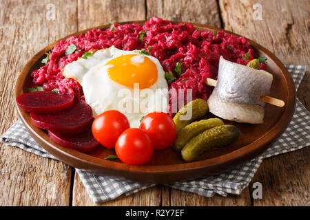 Il pasto tradizionale della Germania del nord Labskaus della fecola di patate, di corned beef barbabietole e serviti con uovo fritto, sottaceti e aringhe close-up su una piastra sul th Foto Stock