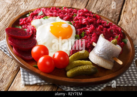 Fatta in Casa Labskaus della fecola di patate, di corned beef barbabietole e serviti con uovo fritto, sottaceti e rollmops close-up su una piastra sul tavolo orizzontale. Foto Stock