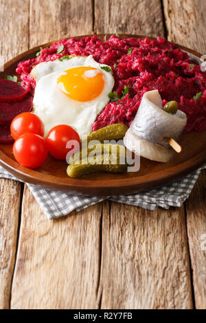 Labskaus tedesco sostanziosa pietanza di fecola di patate, di corned beef e barbabietola con uovo fritto, sottaceti e aringhe close-up su una piastra sul tavolo. In verticale Foto Stock