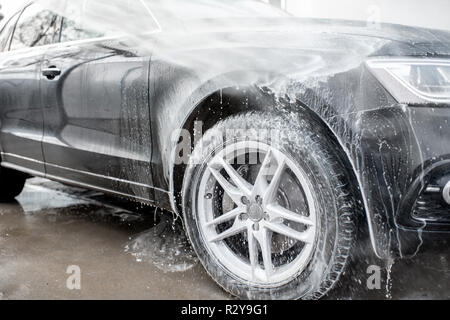 Close-up di un auto sotto il getto di acqua durante il processo di lavaggio su un self service lavaggio auto Foto Stock
