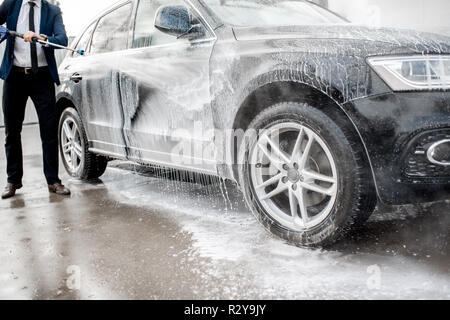 Close-up di un auto sotto il getto di acqua durante il processo di lavaggio su un self service lavaggio auto Foto Stock