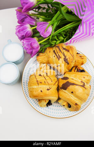 Tre croissant, due tazze di caffè sul tavolo e un mazzo di bellissimi tulipani. Foto Stock