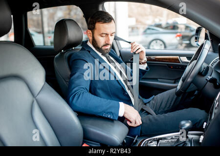 Imprenditore elegante vestito con la tuta il fissaggio della cintura di sicurezza prima di guidare la sua auto Foto Stock