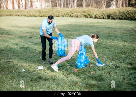 L uomo e la donna volontari Vestito in blu t-shirt pulizia giardino pubblico da rifiuti plastici in sacchi Foto Stock