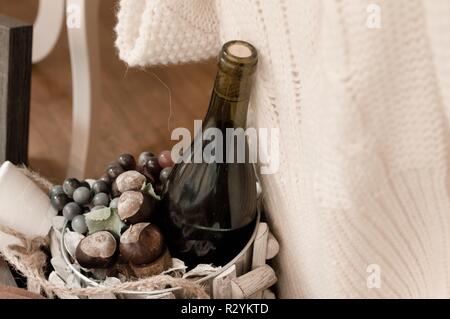 Una bottiglia di vino con le castagne in un basken in legno e un maglione bianco (Marche, Italia) Foto Stock