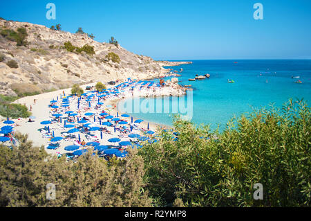 Immagine di Konnos spiaggia nei pressi di Agia Napa, Cipro. Blu molte sedie a sdraio e ombrelloni sulla sabbia bianca nei pressi di blu trasparente di acqua in una baia e le colline rocciose. Foto Stock
