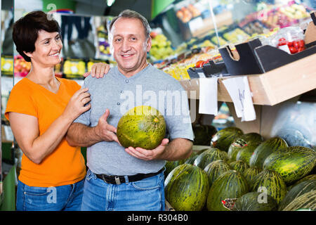 Adulto positivo allegro maschio e femmina sono la scelta di verde di meloni in negozio. Foto Stock