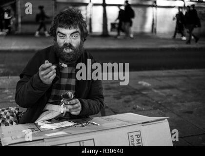 Senzatetto uomo seduto sulla strada di Londra mangiare di una scatola di cartone Foto Stock