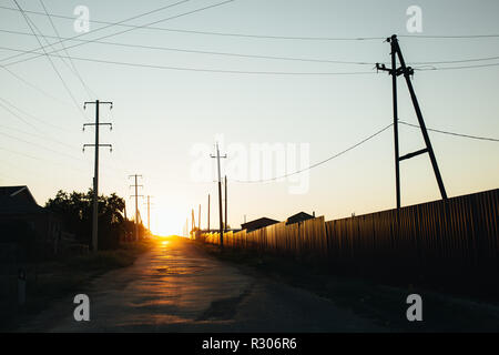 Bassa tramonto sole splende su una strada rurale. Ci sono edifici privati a sinistra della strada Foto Stock