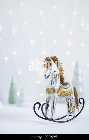 Giocattolo a dondolo cavallo di legno con alberi di Natale e led luci di garland sullo sfondo. Orientamento verticale. Foto Stock