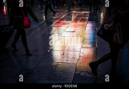 Le persone e i riflessi di luce in un umido Gran Via di Madrid, nel corso di un oscuro nel tardo pomeriggio di domenica. Foto Stock
