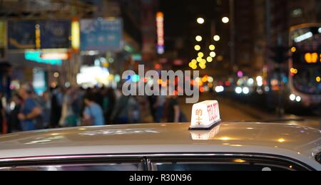 Hong Kong Taxi con illuminato in segno del tetto sulla trafficata strada di notte. Mong Kok, Hong Kong. Foto Stock