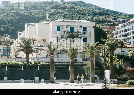 Bella vista della strada di città con edifici di palme e di persone a piedi in Budva in Montenegro. Budva è una popolare destinazione turistica. Foto Stock