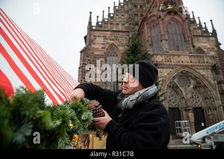 21 novembre 2018, il Land della Baviera, Norimberga: Jürgen Ulrich, stand operatore per old German decorazioni natalizie, vincola una pigna al suo stand di vendita durante la costruzione del Norimberga Mercatino di Natale. Sullo sfondo è possibile vedere la Frauenkirche su cui la galleria Christkind Norimberga sarà aperto il Christkindlesmarkt con il suo prologo su 30.11.2018. Foto: Daniel Karmann/dpa Foto Stock