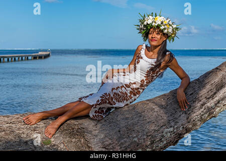 Giovane donna con la ghirlanda di fiori di frangipani poggiando su palm tronco, Raiatea, Polinesia Francese Foto Stock