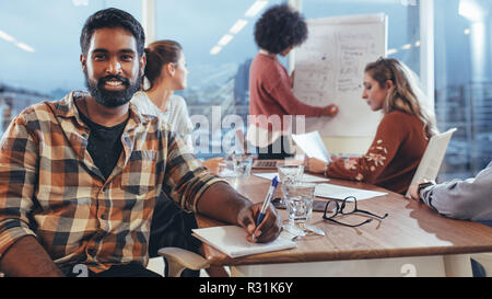 uomo d'affari seduto a una riunione con i colleghi in ufficio. Imprenditrice donna che spiega idee e piani ai colleghi su una lavagna a fogli mobili in lingua originale Foto Stock