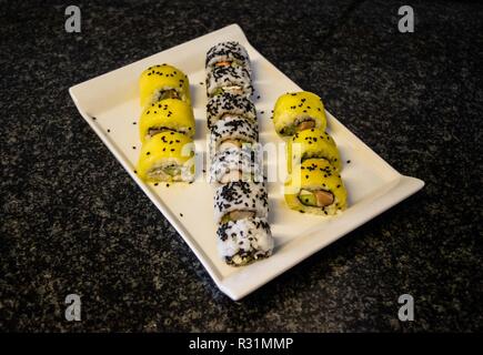 Presentato splendidamente e preparata di fresco di mango dolci rotolo di sushi servita su una piastra bianca, tavola nera, sushi platter Foto Stock