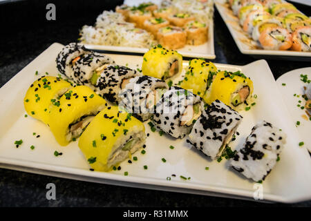 Presentato splendidamente e preparata di fresco di mango dolci rotolo di sushi servita su una piastra bianca, tavola nera, sushi platter Foto Stock
