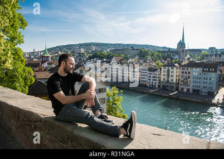 Bel giovane ragazzo seduto nel parco della città con una vista della città di Zurigo, Svizzera. Foto Stock