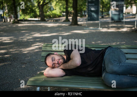Bel giovane uomo barbuto è dormire su una panchina nel parco Foto Stock