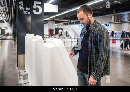 Giovane uomo usando self i chioschi di check-in in aeroporto. Foto Stock