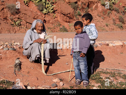 Marrakech, Marocco - 21,02,2012: un anziano, tipicamente vestito uomo berbero con i suoi nipoti cinghie di artigianato della paglia in Alto Atlante. Foto Stock