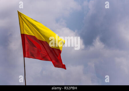 Belur, Karnataka, India - 2 Novembre 2013: Giallo e rosso bandiera di stato sul polo galleggianti contro il cielo blu con nuvole bianche. Foto Stock