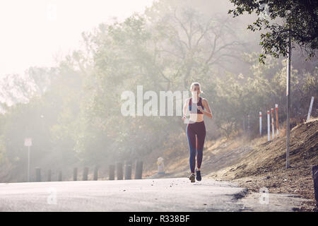 Bella bianco caucasico donna corre lungo la strada del sole del mattino Foto Stock