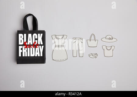 Vista superiore della carta nera Borsa con venerdì nero vendita iscrizione e vestiti di carta su sfondo grigio Foto Stock