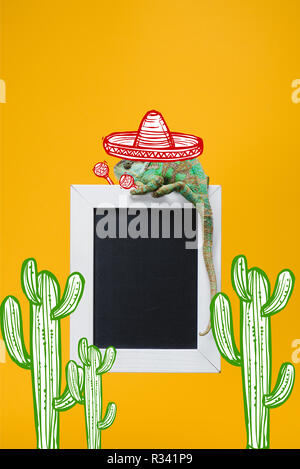 Bella camaleonte colorate in sombrero hat con le maracas sulla lavagna isolati su giallo con cactus messicani Foto Stock