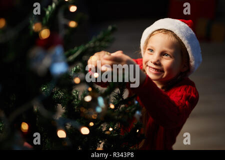 Felice ragazza Appendere le decorazioni di Natale sul ramo di abete durante la preparazione per la celebrazione Foto Stock