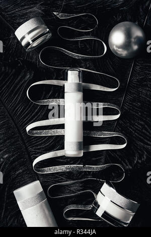 Vista in elevazione d'argento palla di Natale, un trattamento di bellezza attrezzature, nastro sulla superficie con piume nere Foto Stock