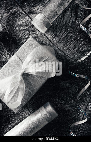 Vista superiore del regalo di Natale scatola, lozione, acqua micellare e nastro sulla superficie con piume nere coperte da argento Foto Stock