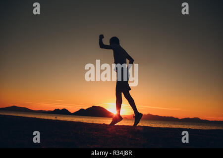 Giovani energico uomo felice jumping in riva al mare Foto Stock
