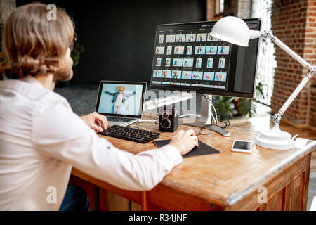 Giovane maschio fotografo lavorando con una donna ritratti seduti al posto di lavoro con due computer in studio Foto Stock