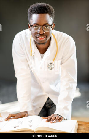Ritratto di un giovane africano di etnia medico o studente di medicina in uniforme durante il lavoro o lo studio in ufficio o a scuola Foto Stock
